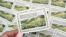 Load image into Gallery viewer, A hand with light pink manicured nails holds a single decorative card with a green and white botanical illustration and text, while several identical cards are scattered on a dark wood surface.