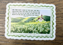 Load image into Gallery viewer, A vintage-style religious prayer card with a white scalloped border and a green inner border, featuring a pastoral landscape illustration of a church in a flower field and a Bible verse from Psalm 27:4. The card is photographed on a rustic wooden surface.
