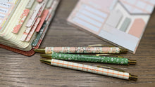 Load image into Gallery viewer, Three decorative pens on a wooden surface with stationery items in the background