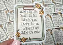 Load image into Gallery viewer, A hand holds a die-cut Bible verse sticker in the foreground, with several matching stickers scattered on a dark wooden surface in the background.
