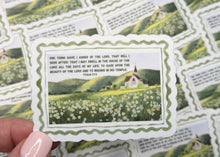 Load image into Gallery viewer, A hand with light pink manicured nails holds a rectangular decorative card featuring a green tea plantation scene with white flowers and printed text. Multiple identical cards are scattered on a dark wooden surface in the background.